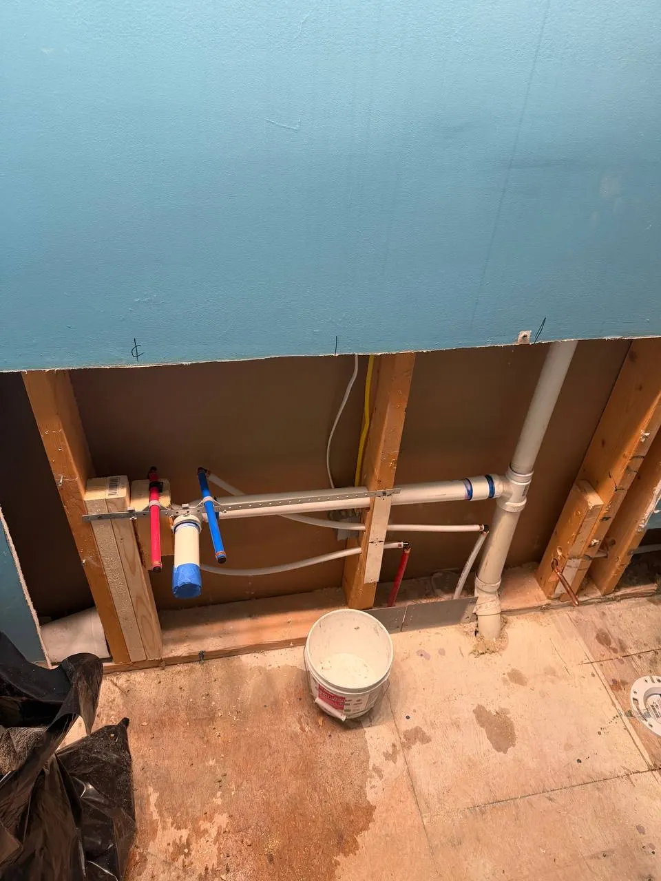 Opened wall showing the relocated vanity drain, hot and cold supply stub-outs and new PVC waste and vent piping