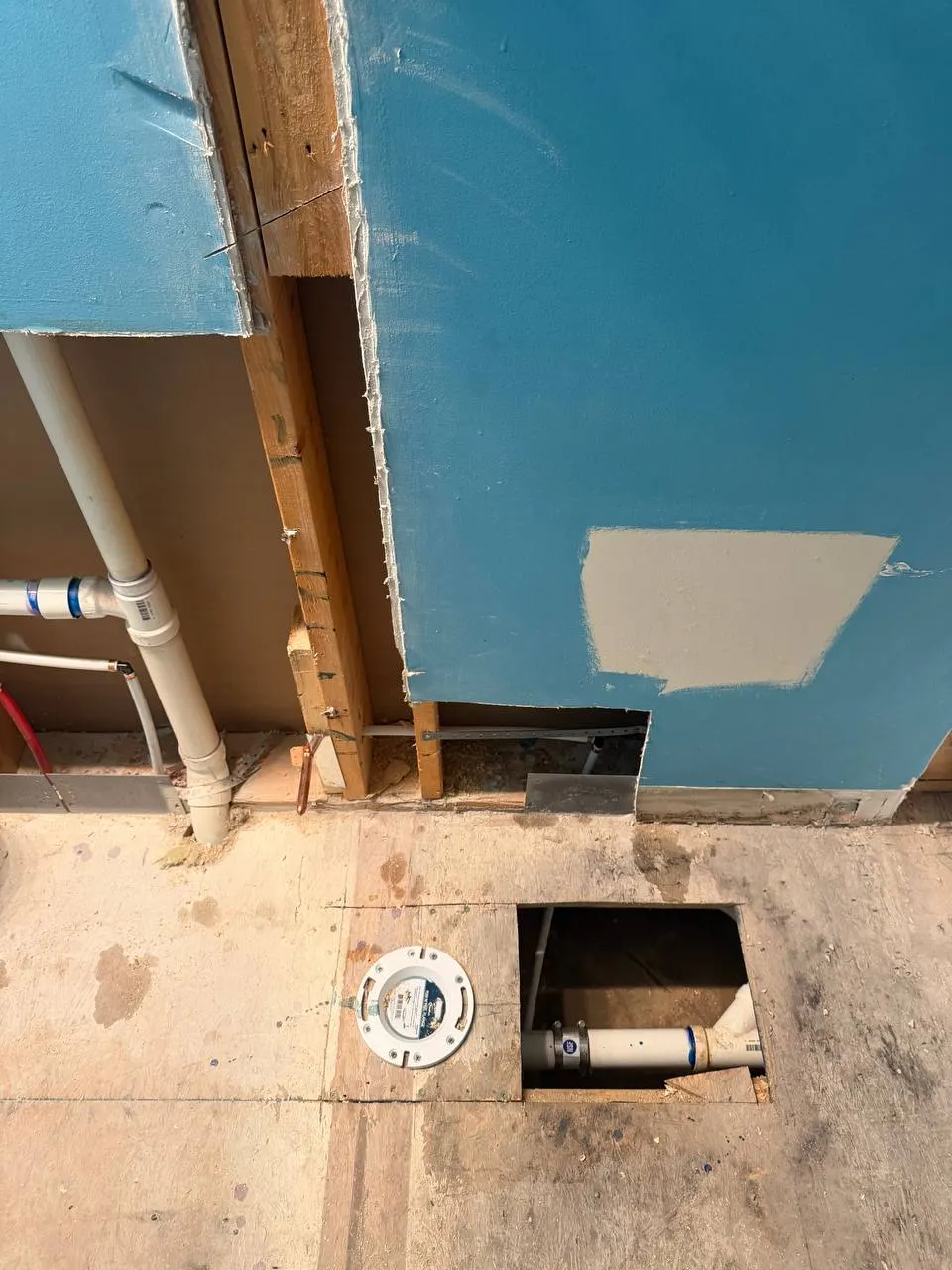 Relocated toilet flange set in the subfloor next to an opening showing the new drain connection below
