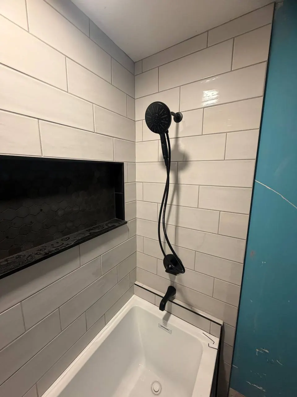 Finished tub and shower with white subway tile, a black shower head, handheld attachment and matching tub spout