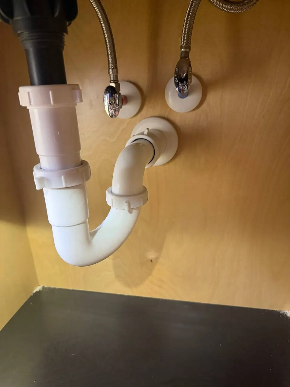 Vanity plumbing under the sink with a white P-trap, chrome shutoff valves and braided supply lines