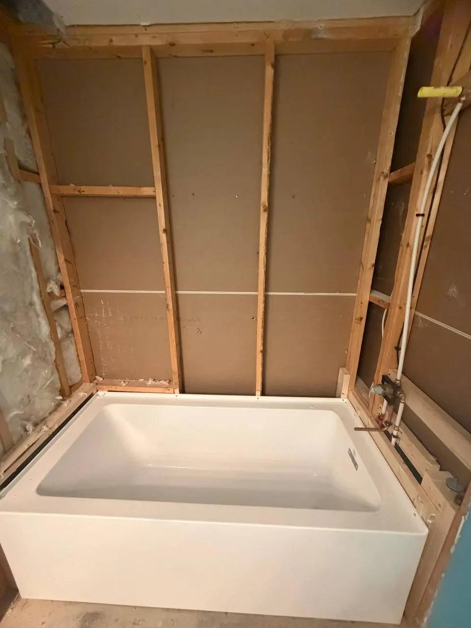 New white bathtub set in the framed alcove before tiling, with the shower supply piping at the right