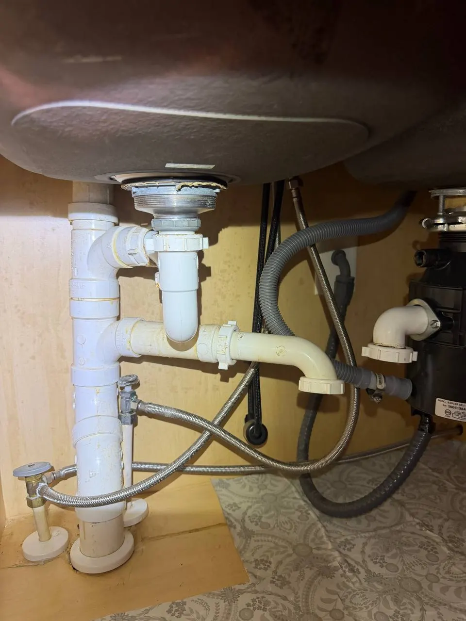 The original under-sink plumbing for the double-bowl sink, with two tailpieces and the disposal at the right