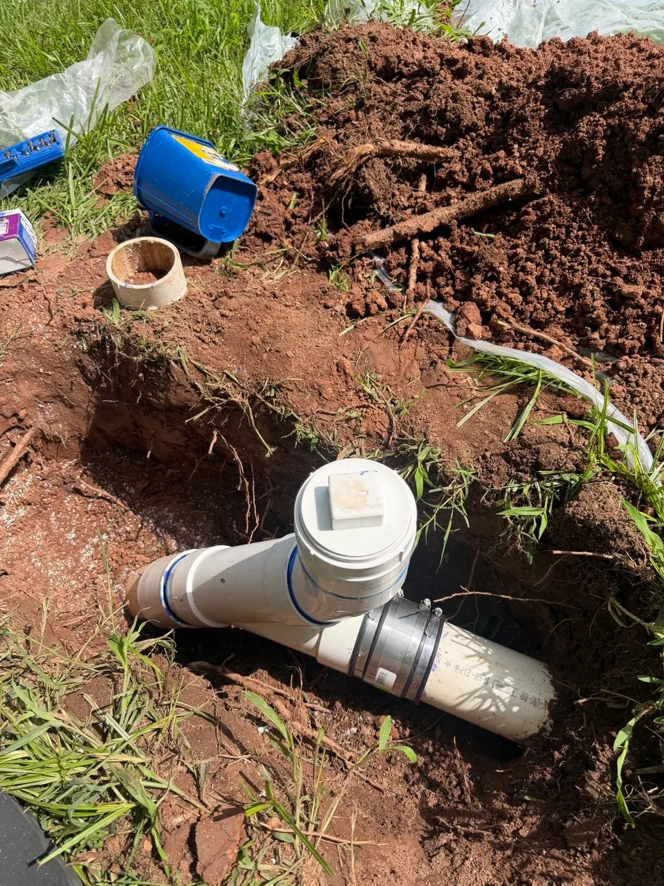 New PVC cleanout tee with a threaded plug, joined to the existing sewer pipe with a banded coupling in the open excavation