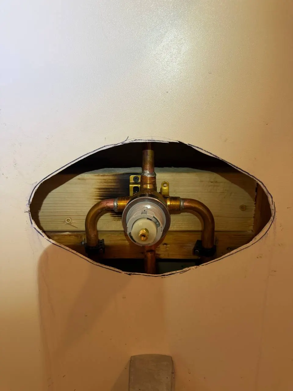 New rough-in valve secured to wood backing, with copper supply, shower riser and tub spout connections visible through the enlarged opening