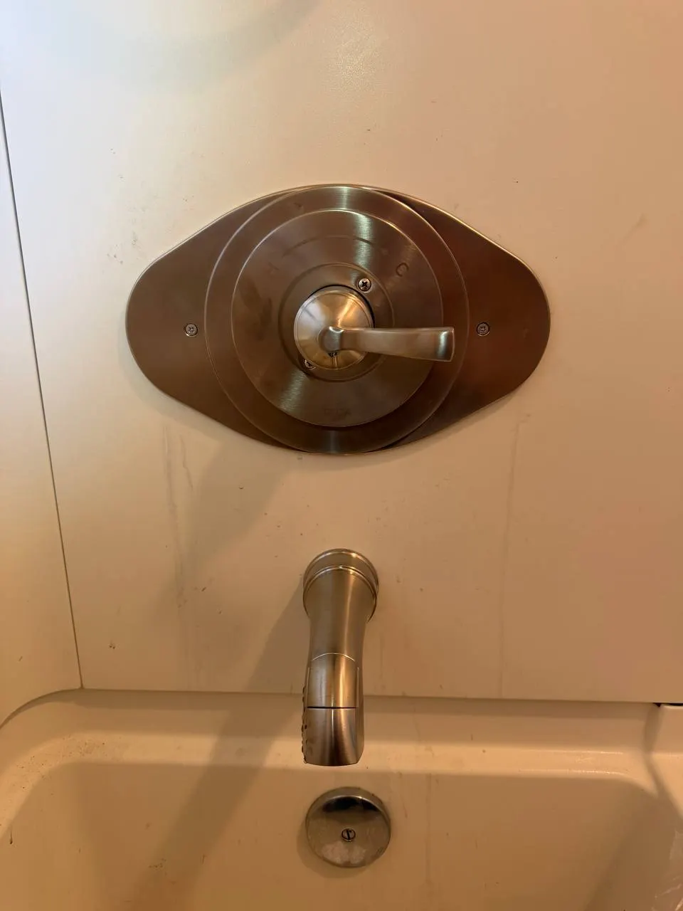 Finished brushed nickel shower trim on an oval remodel cover plate, with a matching tub spout above the bathtub