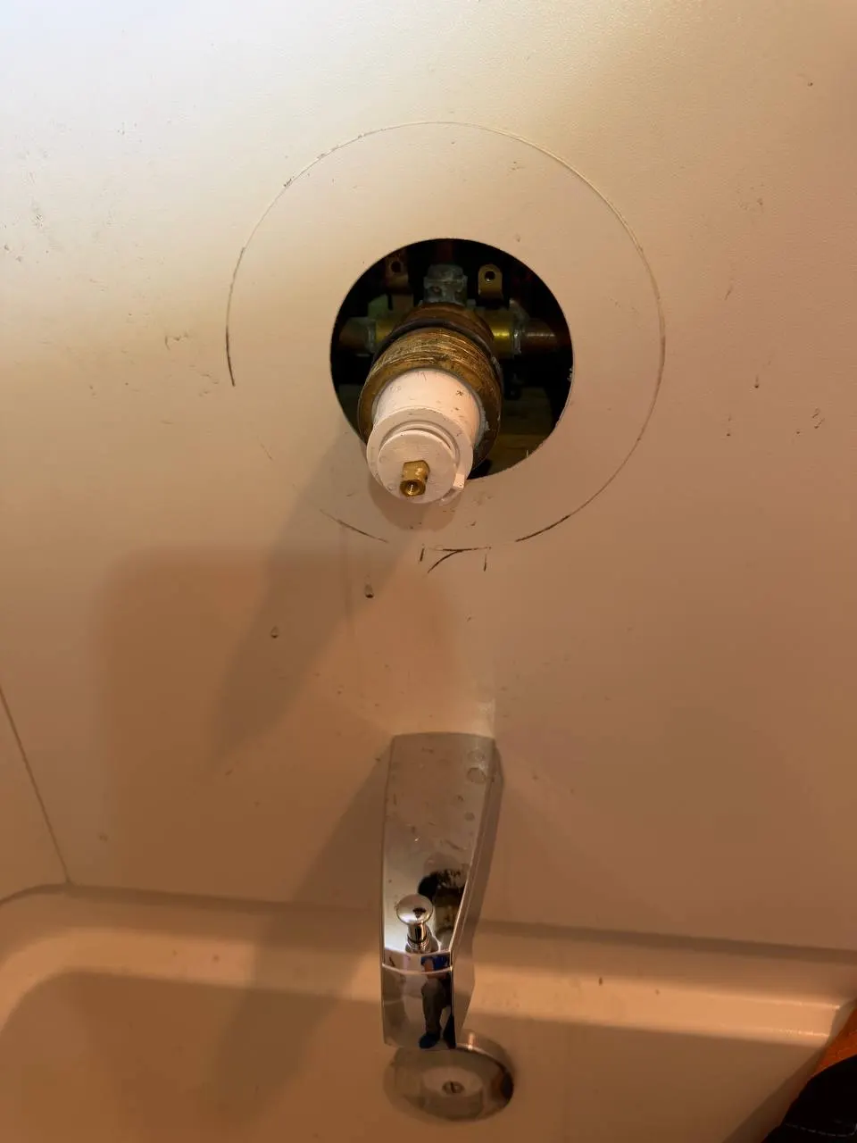 The old shower valve visible through a round opening cut in the shower surround, with the original tub spout below